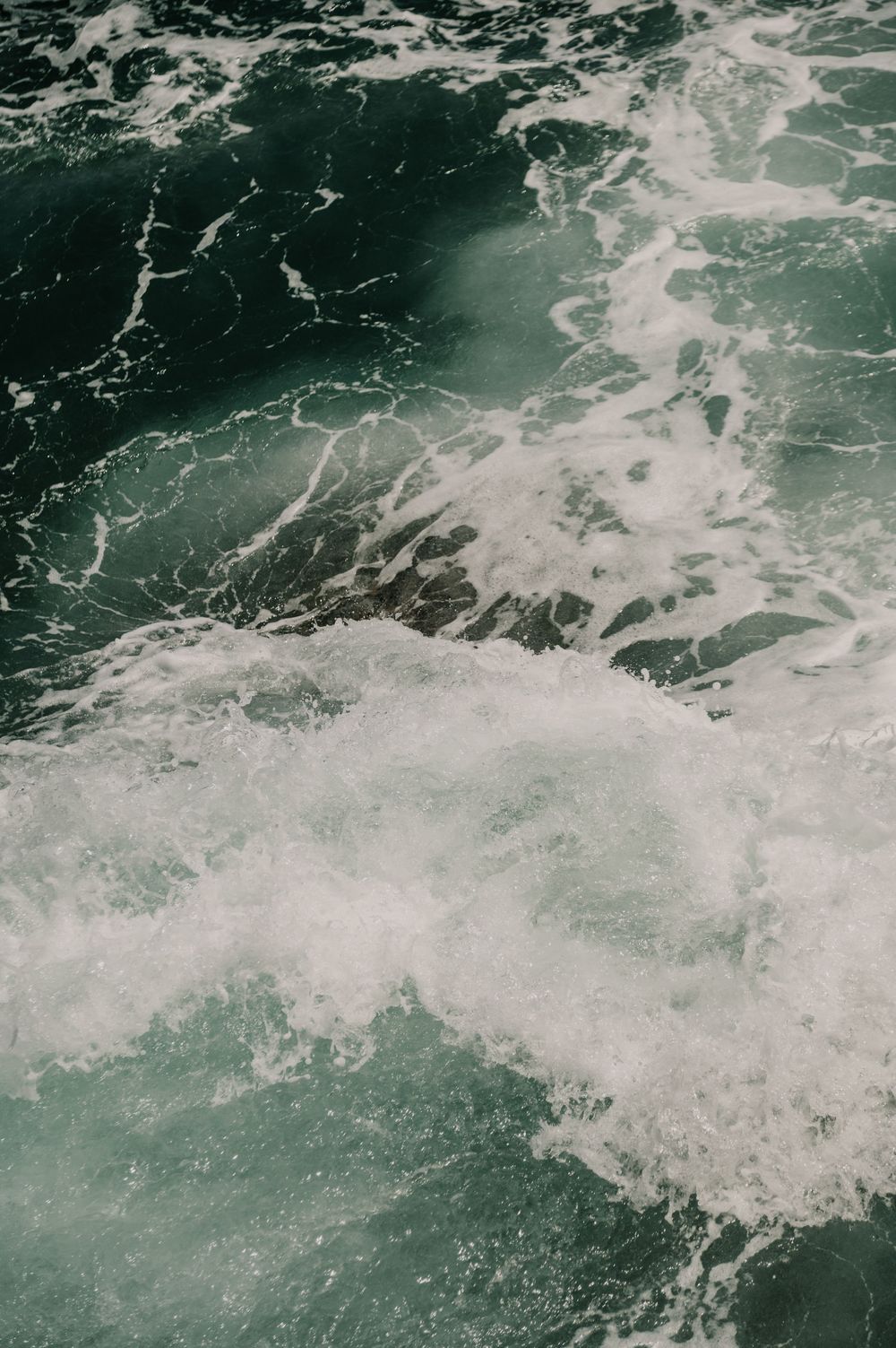 Churning ocean waves create white foam patterns in dark teal waters.