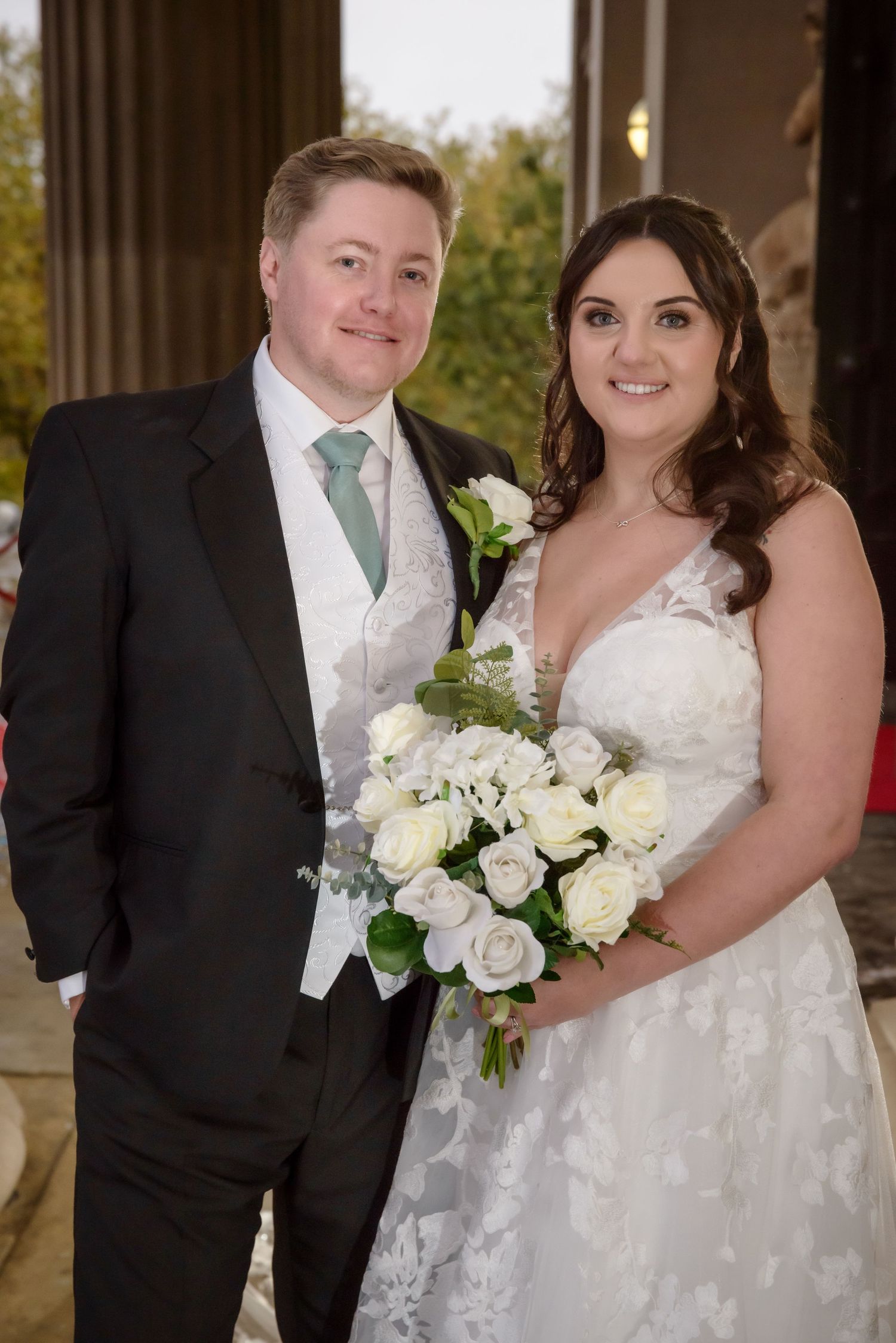 A bride and groom pose together at their wedding, with the bride holding a white rose bouquet at St. George's Hall in Liverpool