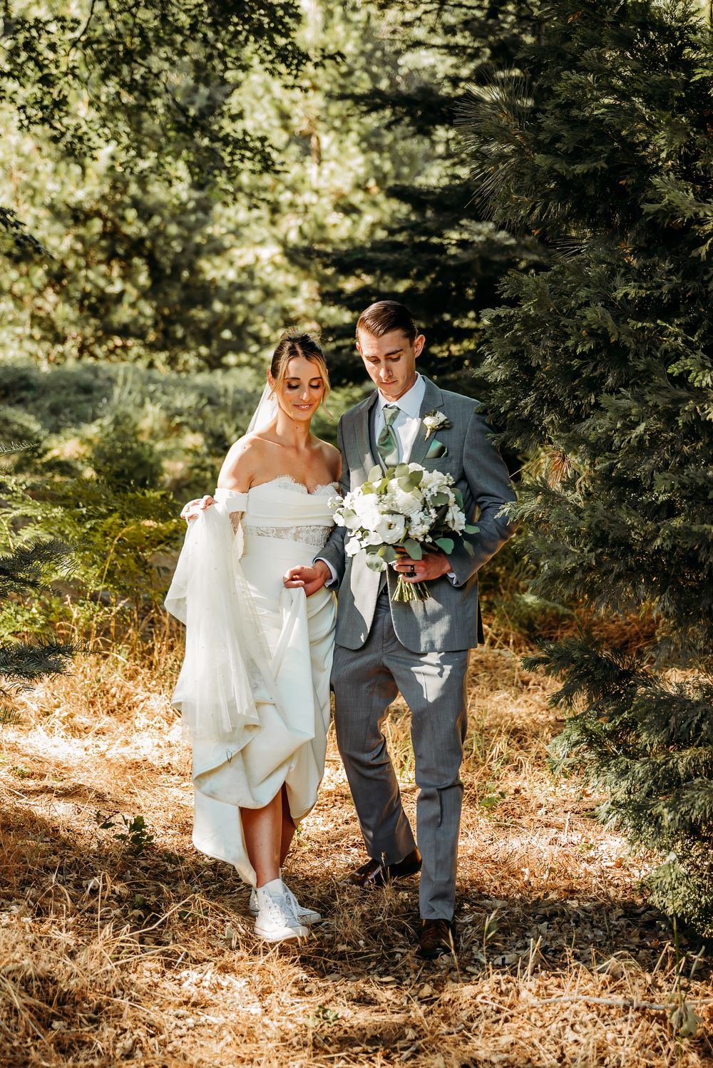 Couple in wedding attire walking together on sun-dappled autumn leaves.