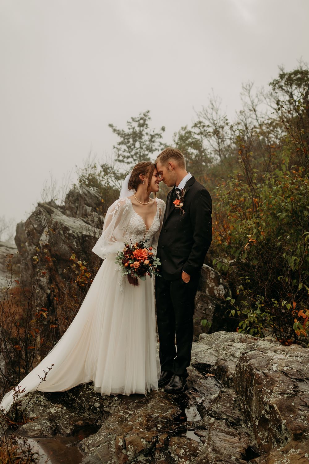 Couple standing on a rock with bushes behind them.