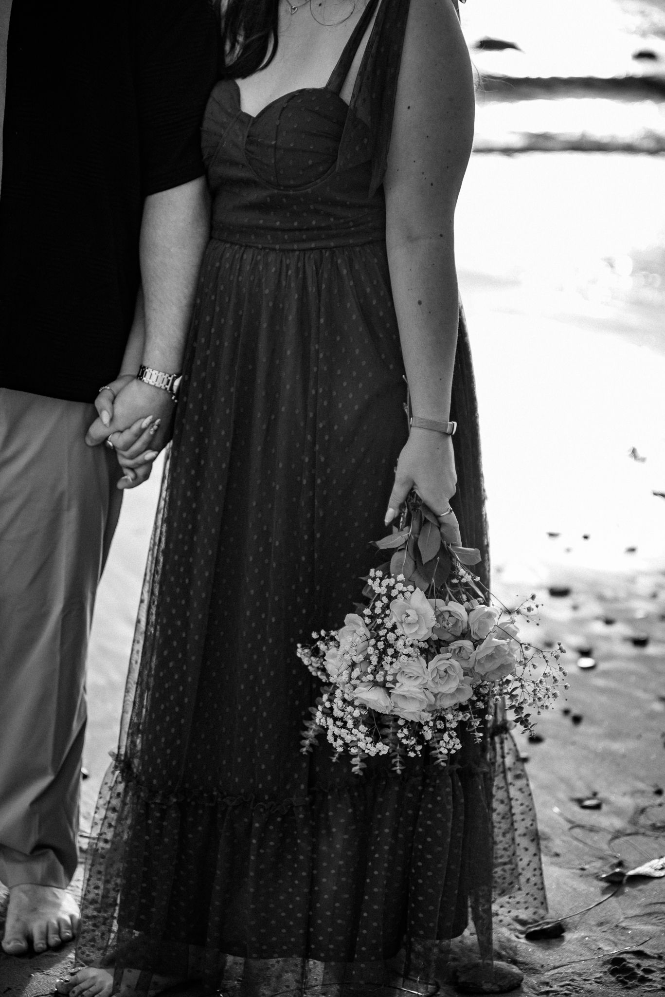 Picture of a couple holding hands while in the other hand the female is holding a bouquet of flowers.