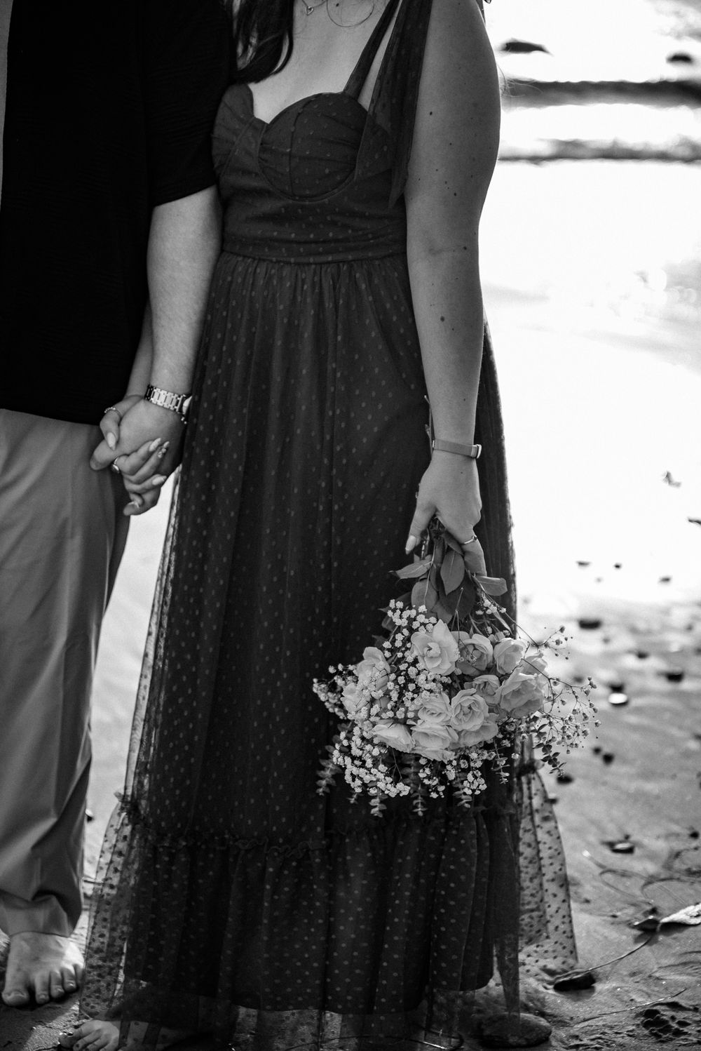 Picture of a couple holding hands while in the other hand the female is holding a bouquet of flowers.