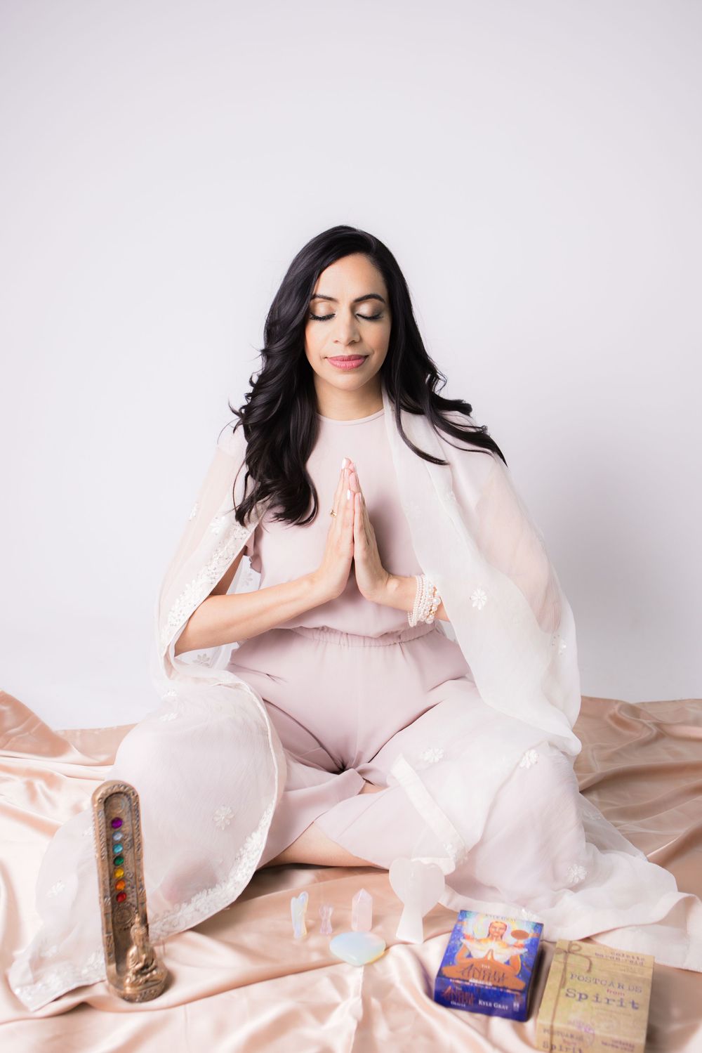 Woman in pink dress lounges on floor with books and blankets in dreamy lifestyle photoshoot.