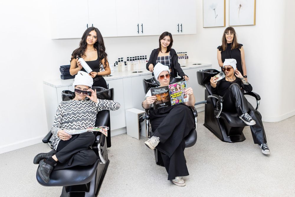 Three people sit in salon chairs reading magazines while waiting at a modern beauty salon.