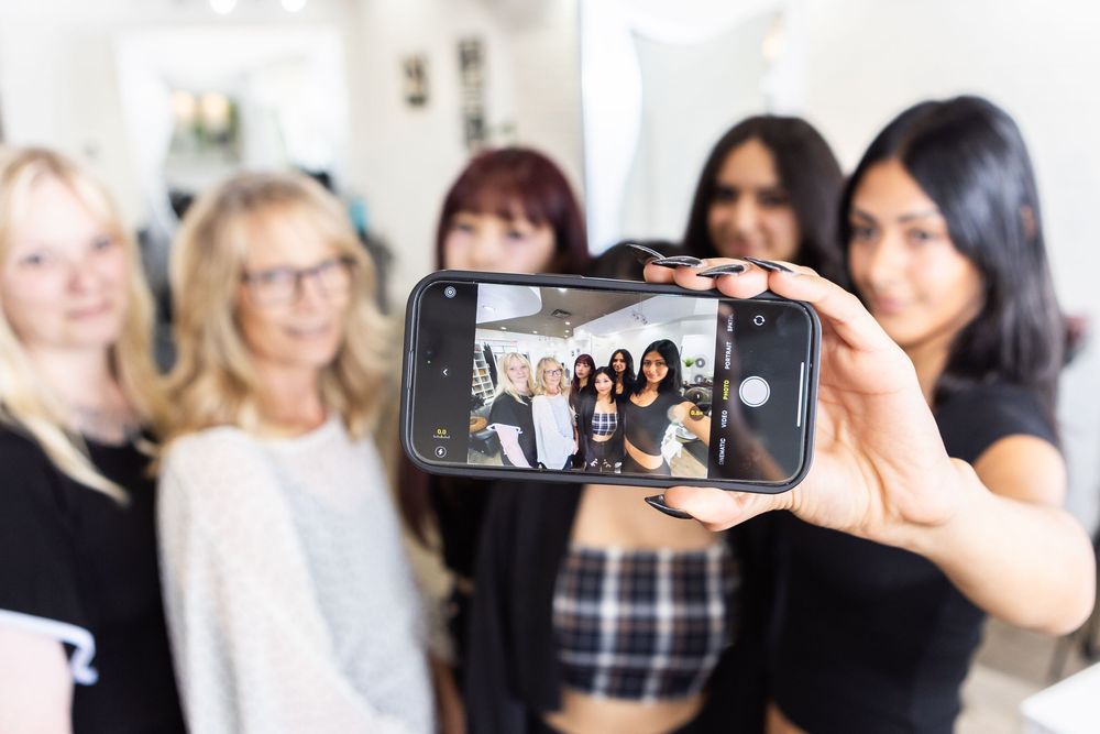 People taking group selfies and photos together at a social gathering using smartphones and cameras.