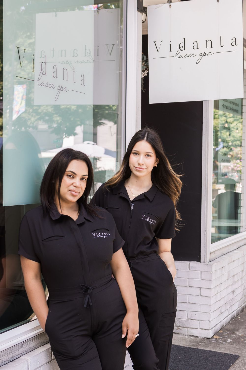 Two staff members wearing black uniforms stand together outside a storefront with white signage.