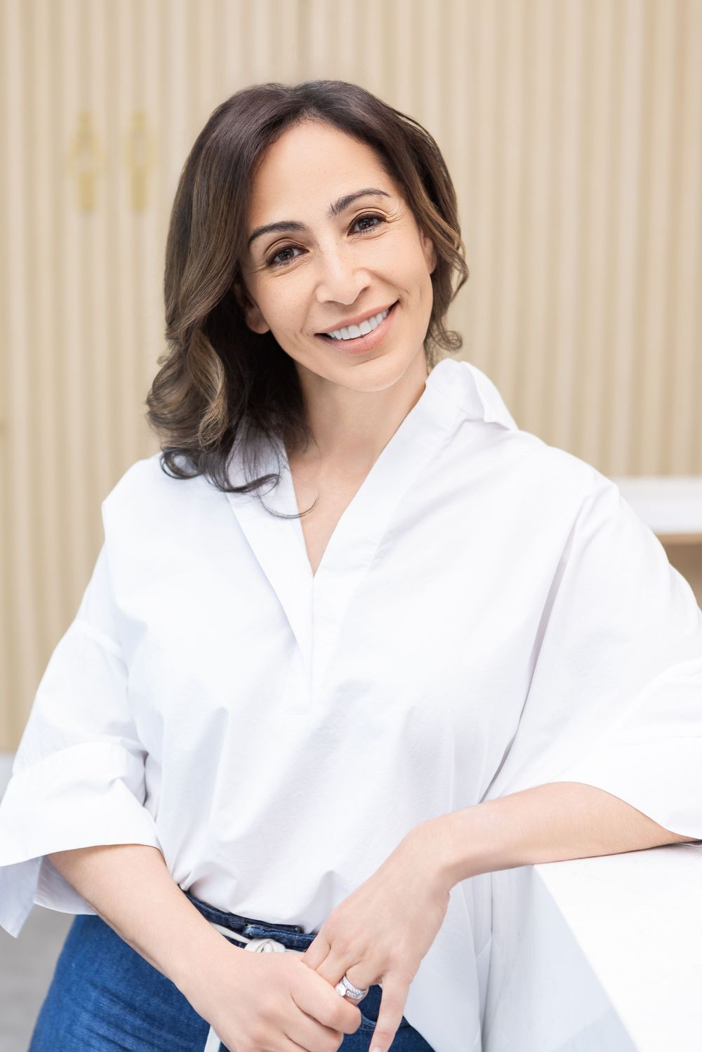 Healthcare professional in white coat sitting with a friendly expression in a medical office setting.