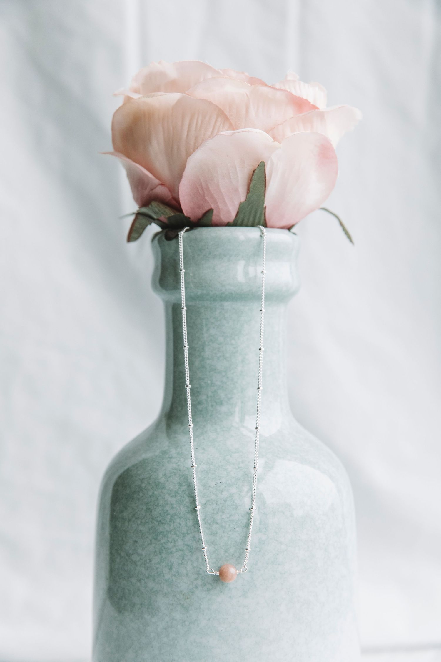 Delicate pink rose in a frosted mint green glass vase against white background.