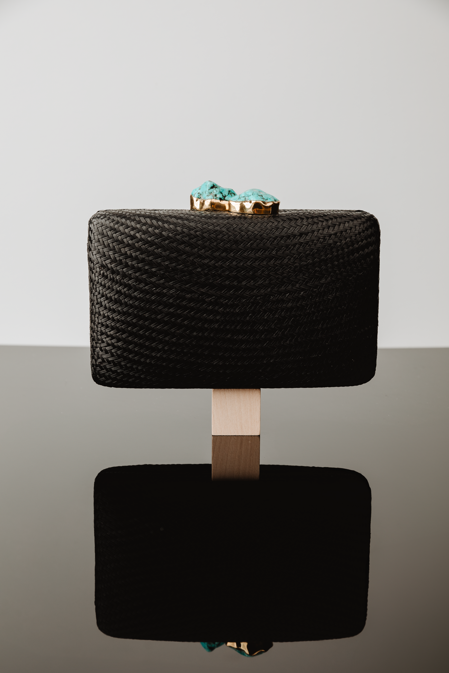 A black woven clutch purse with gold hardware and turquoise accents shown from multiple angles on a light gray background.