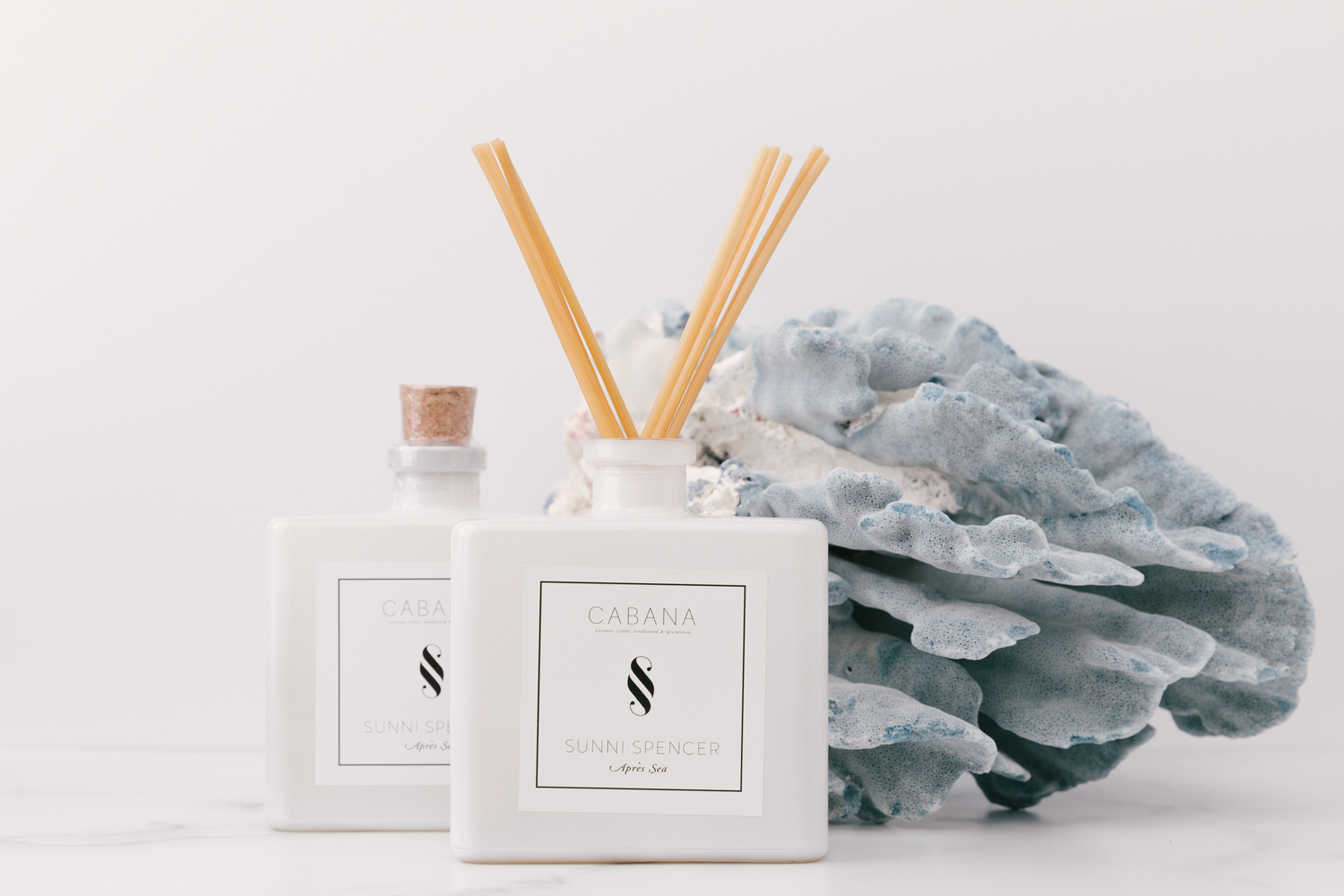 White home fragrance diffusers and decorative coral on light marble surface with minimalist aesthetic.