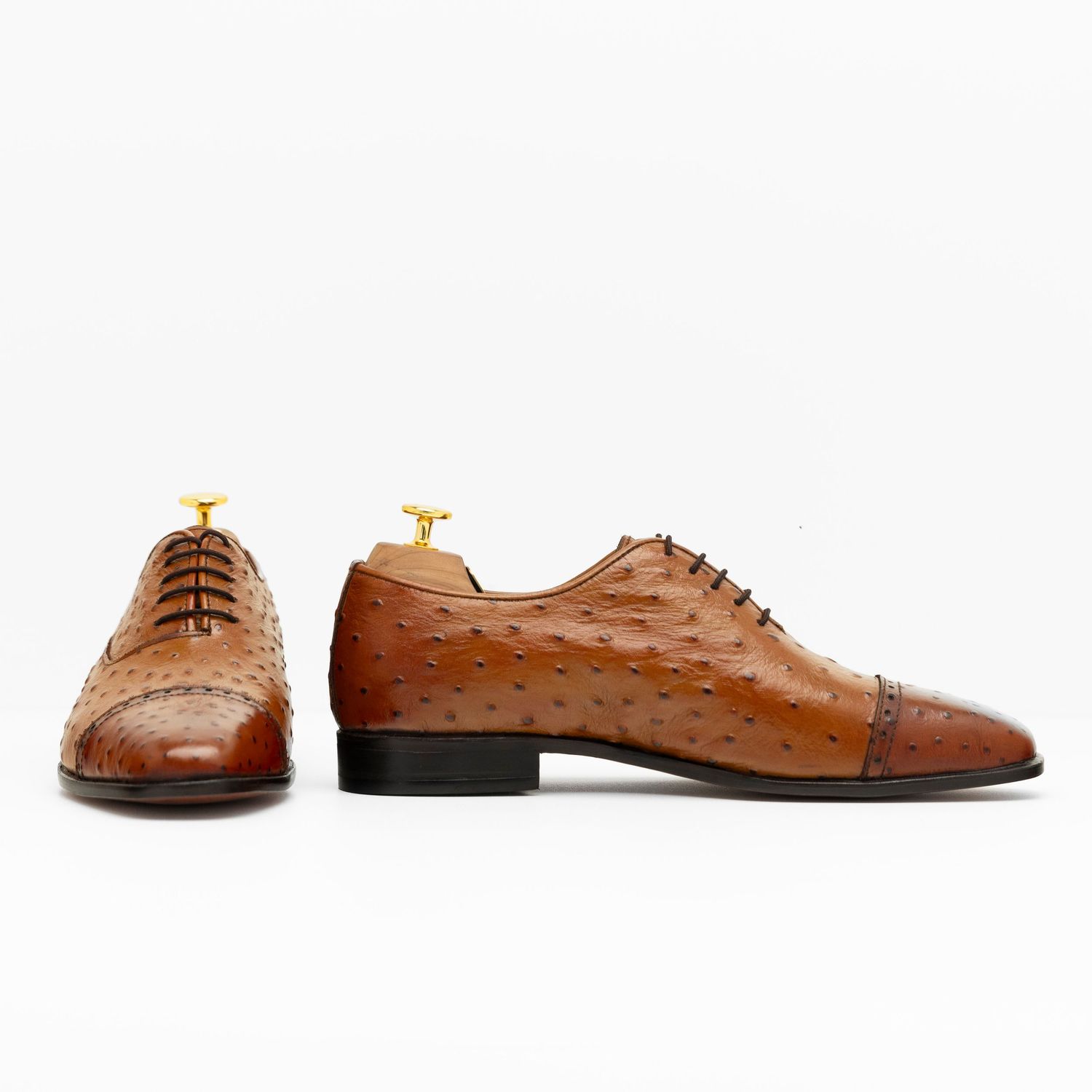 A pair of brown ostrich leather oxford dress shoes with cap toe detailing and black soles displayed on white background.