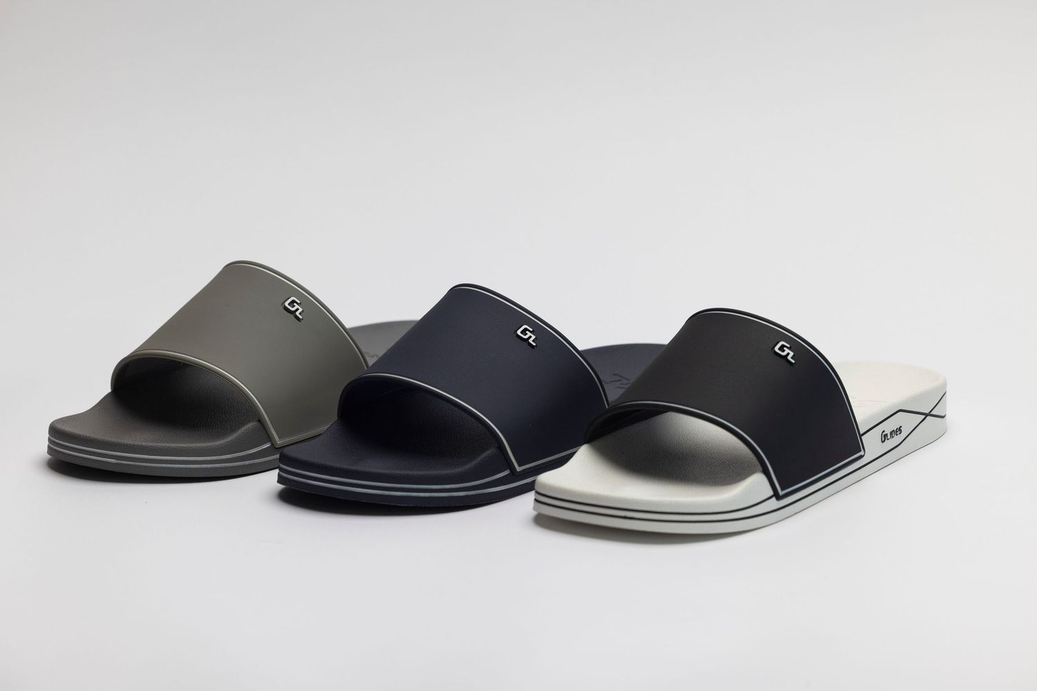 Three casual slide sandals in olive green, navy blue, and metallic silver arranged in a row on white background.