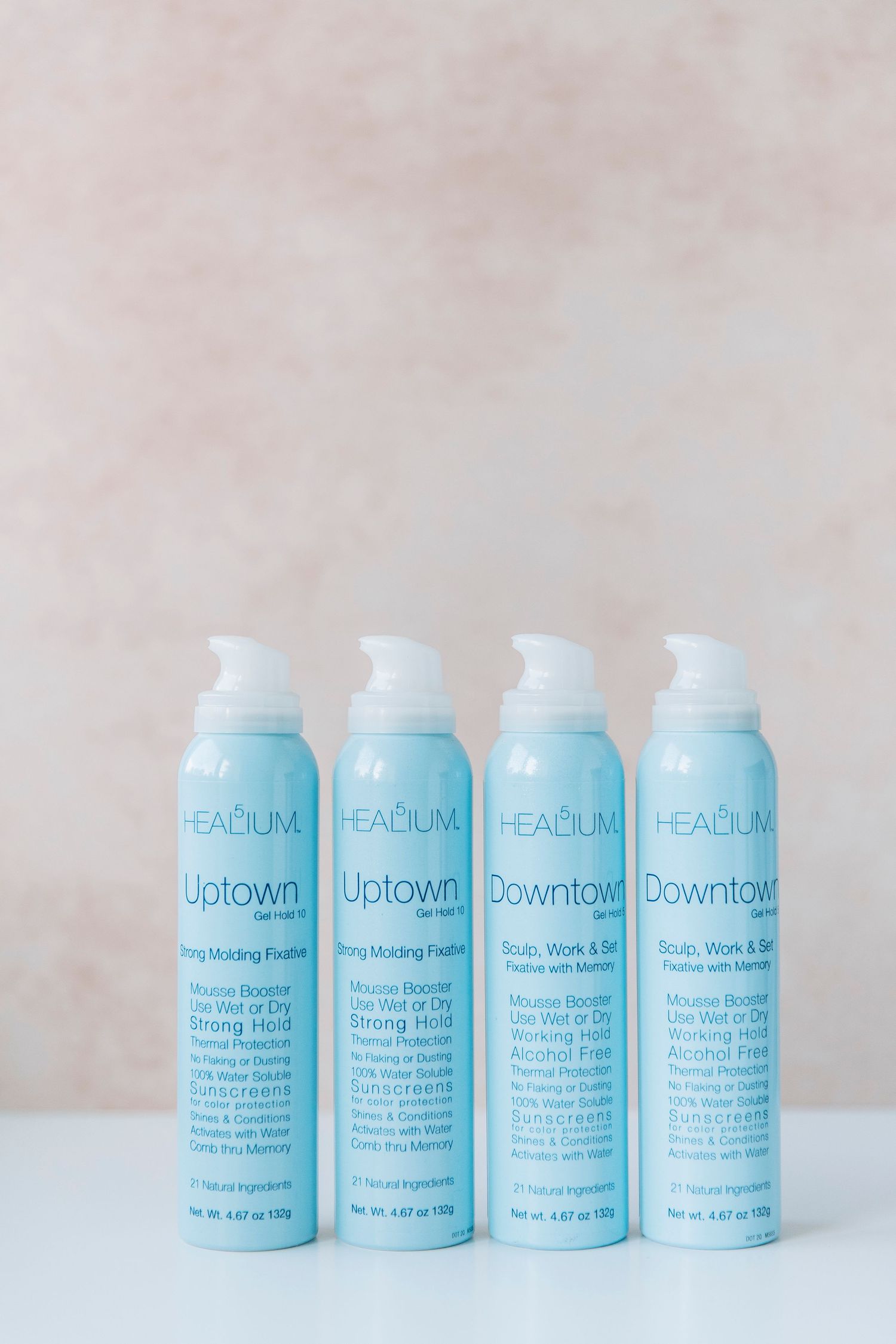 Four light blue hair styling product bottles lined up in a row against a neutral beige background.
