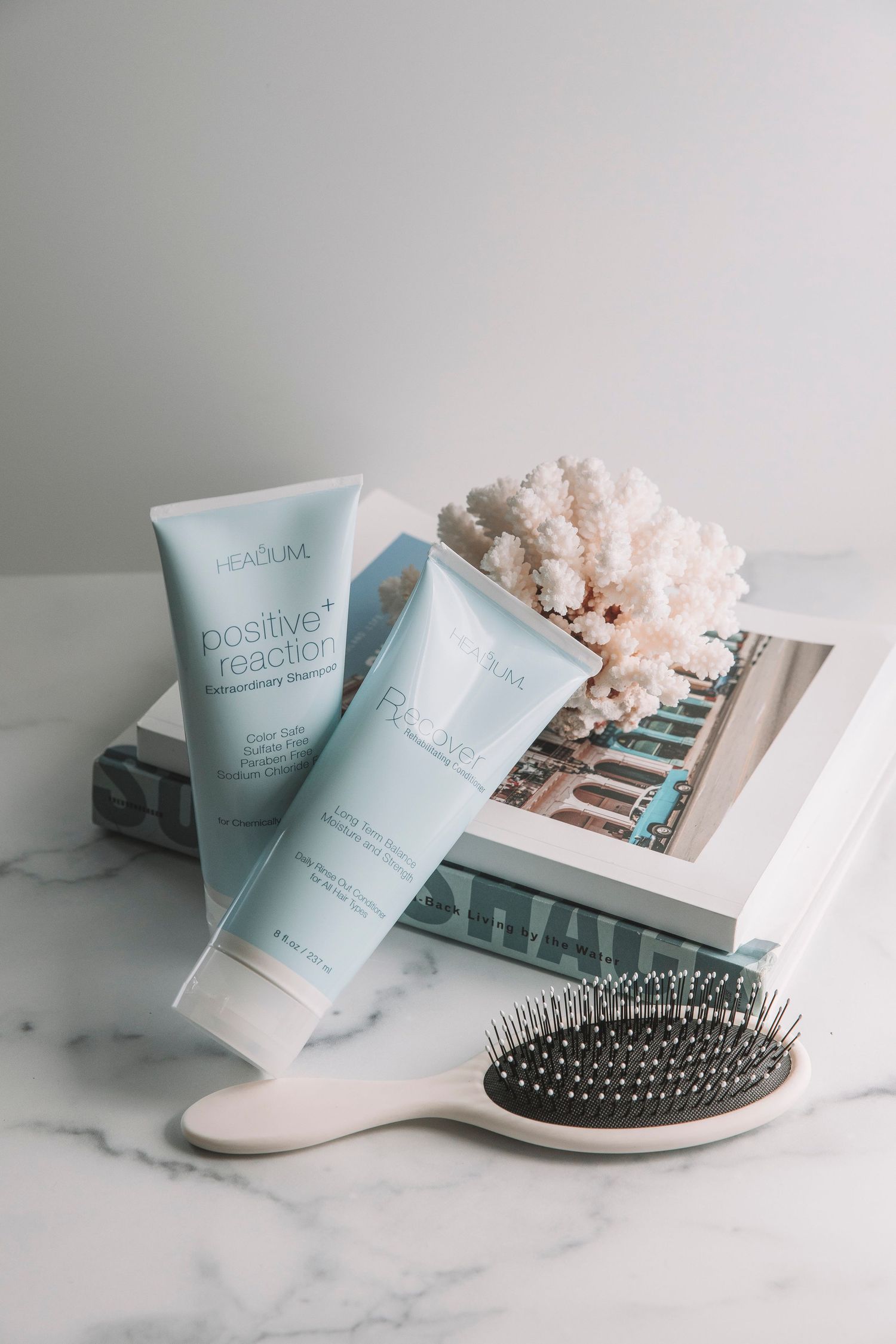 Beauty products and hair brush arranged on marble surface with soft pastel blue packaging and photo prints.