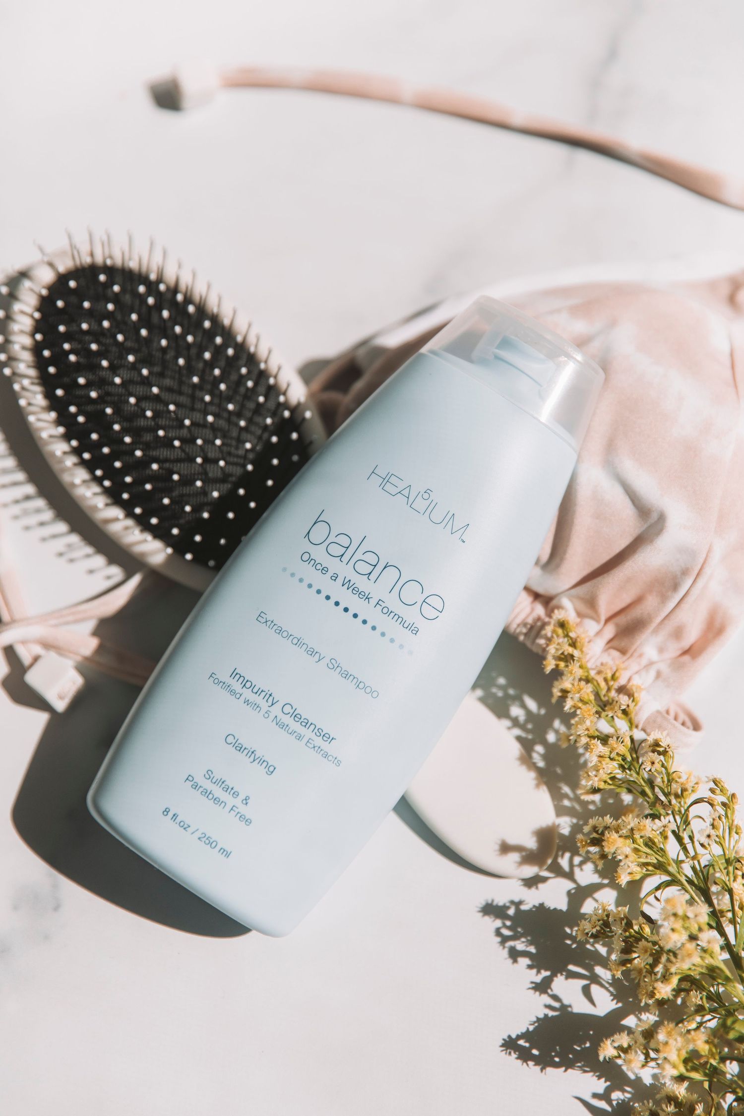 Headium Balance hair product displayed with hairbrush and yellow flowers on white surface.