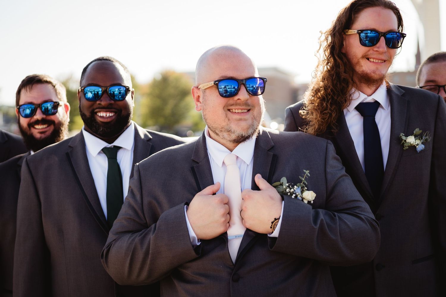 A group of people wearing sunglasses and dark suits pose together outdoors in a formal setting.