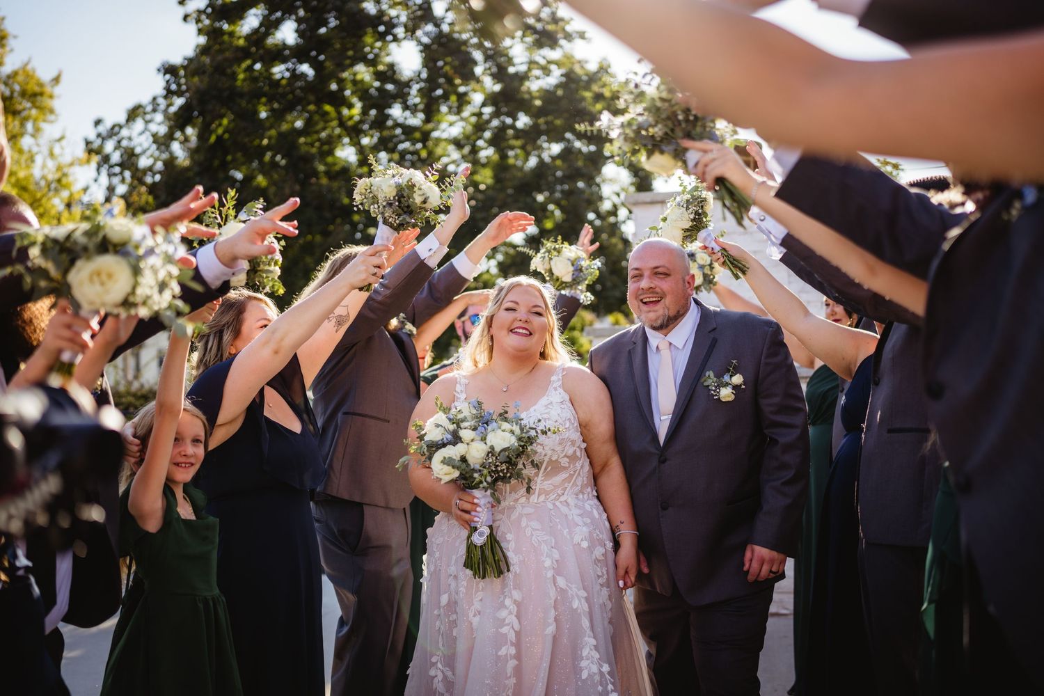 Wedding party celebrates outdoors by tossing flower petals in the air during a joyful ceremony exit.