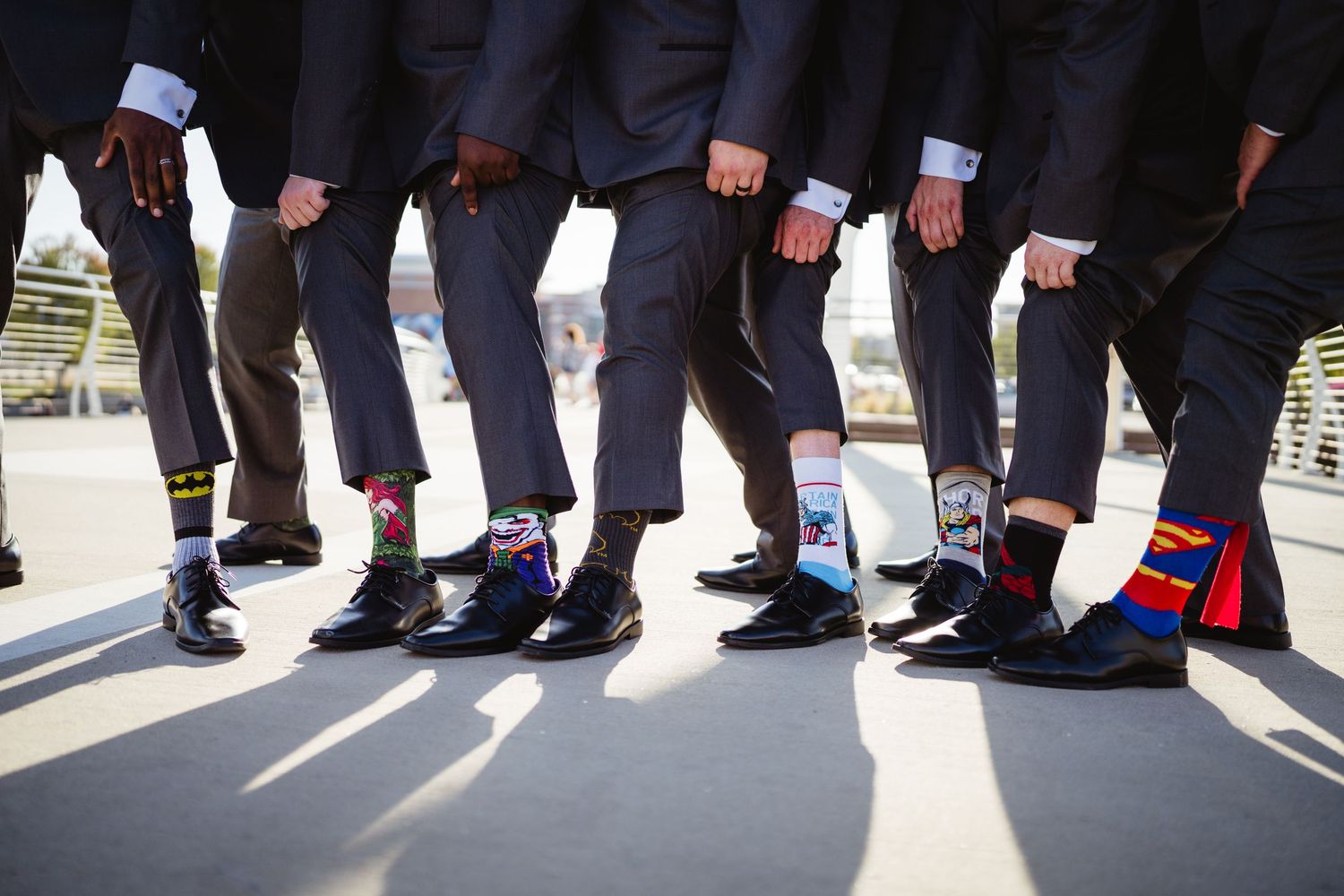 A row of people's legs and feet standing in line against a white background with shadows cast on the floor.