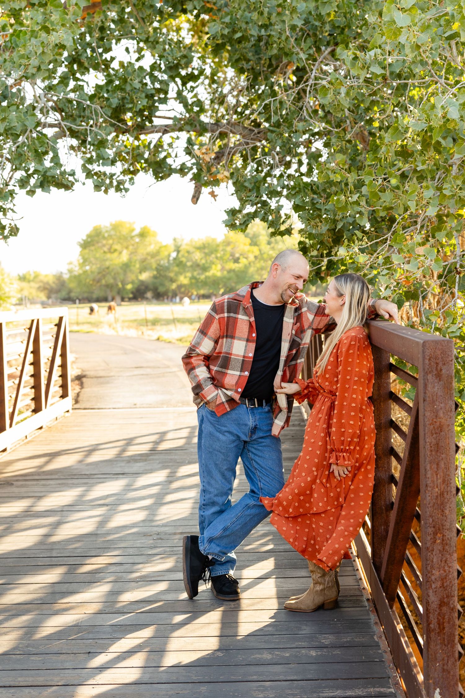 a man looking at a woman lovingly standing on a bridge with the green trees in the background