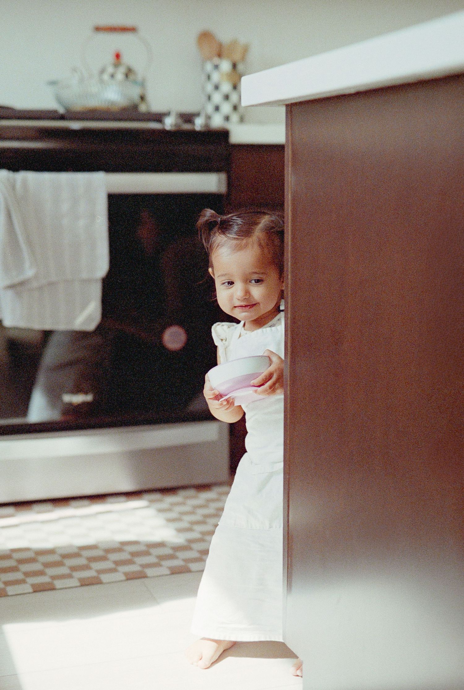 A small child in a white dress peeks around a corner in a sequence of vintage-style film photographs.