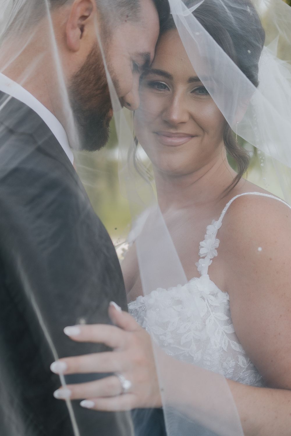Bride smiling under her veil while embracing the groom in an intimate wedding portrait.