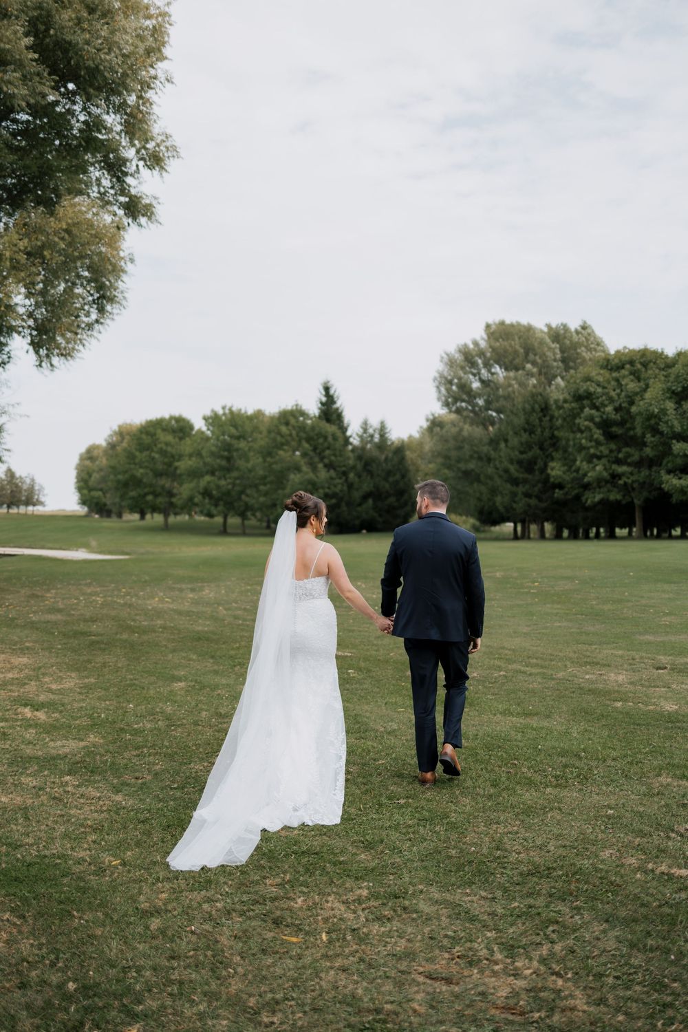 Bride and groom walking hand in hand across a green golf course in wedding attire.