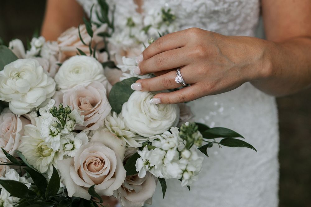 Close-up of a bride holding a white and blush rose bouquet with a diamond engagement ring.