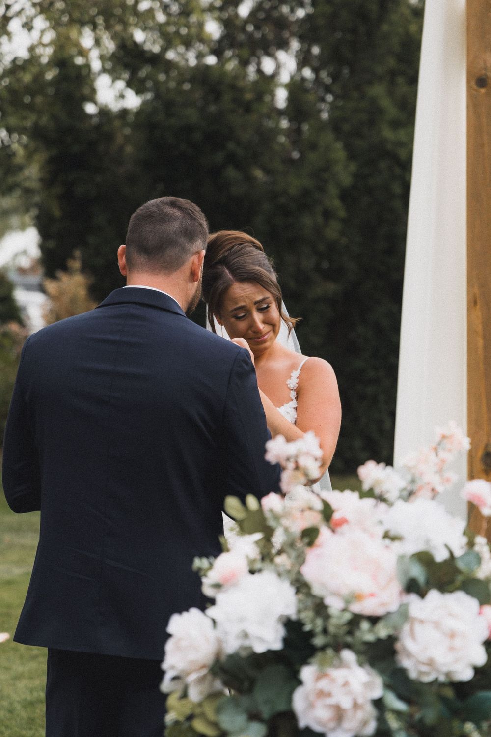 Emotional bride exchanging vows with groom at an outdoor altar adorned with pink florals.