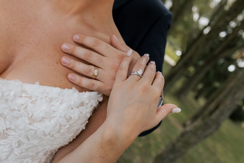Close-up of bride and groom wedding rings on hands resting against white lace wedding dress.