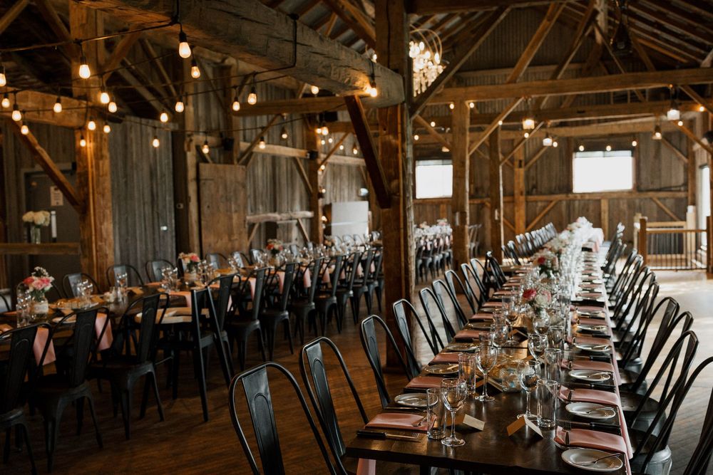 Rustic barn wedding reception venue with long tables, black chairs, string lights, and elegant place settings.