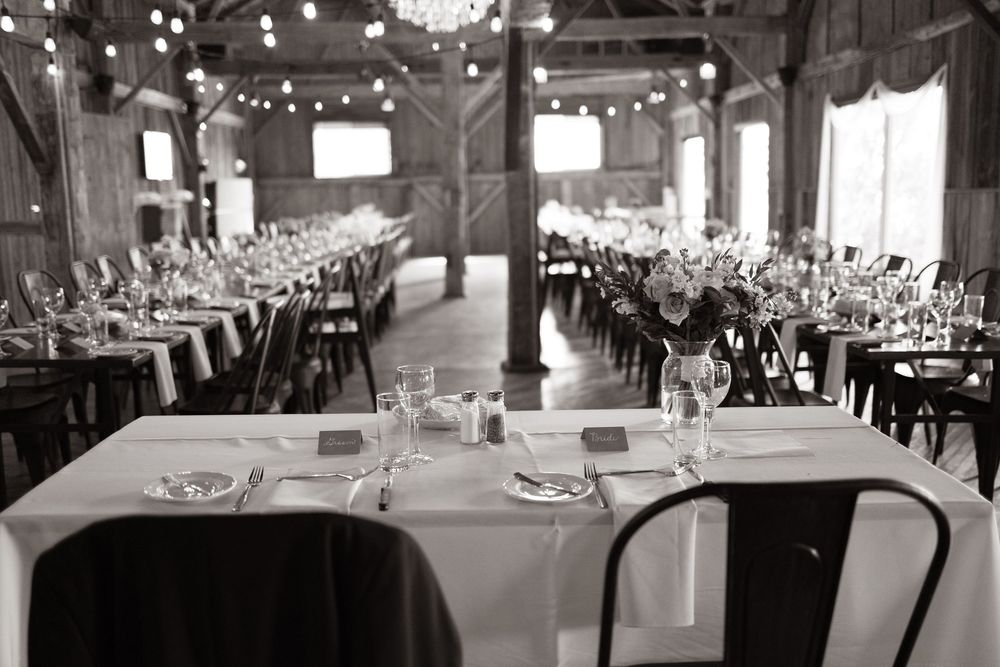 Black and white photo of elegant barn wedding reception tables set with glassware and white linens.