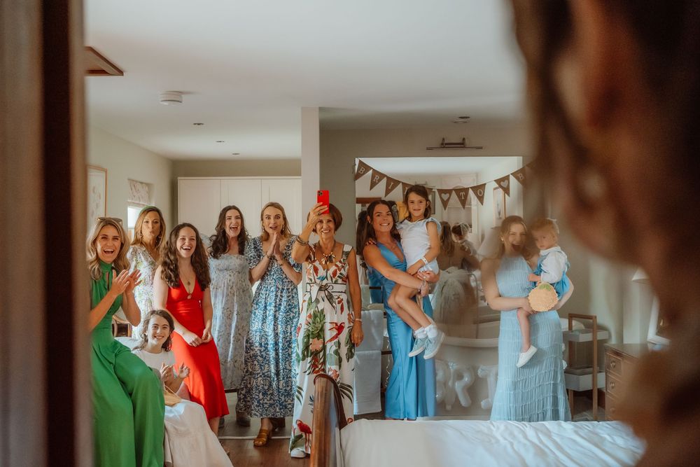 A group of women wearing different colored dresses stand together in a row at what appears to be a wedding event.