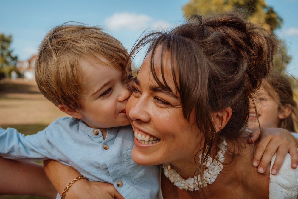 A tender moment of affection and joy captured outdoors on a sunny day with warm lighting.