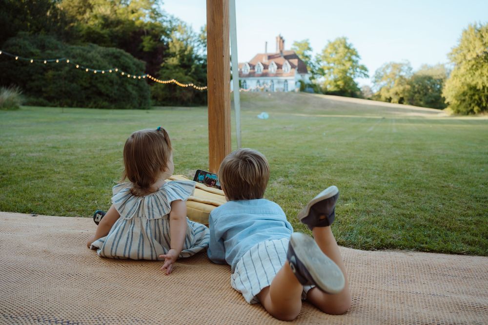 Two people sit close together on a wooden deck overlooking a grassy hillside at sunset.
