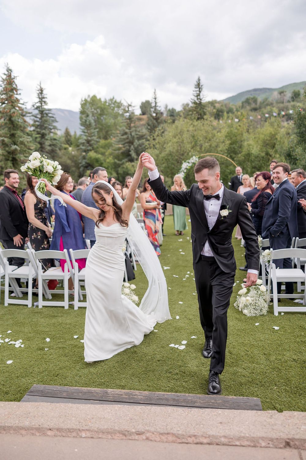 Wedding guests celebrate and dance together on a grassy outdoor venue with mountains in the background.