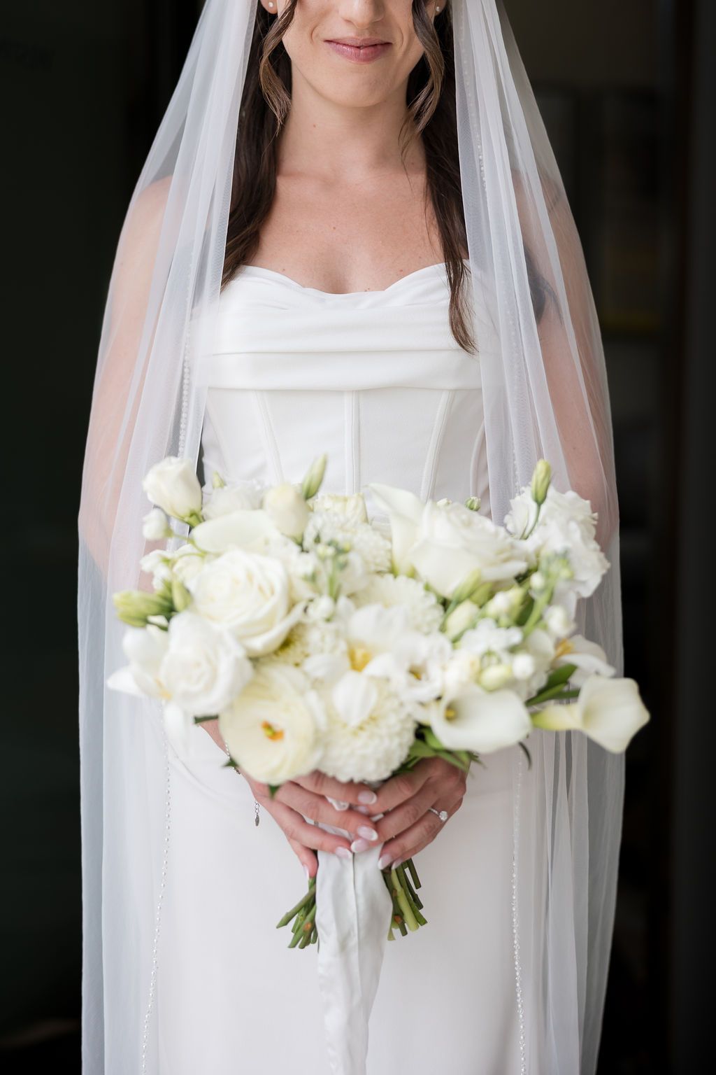 A bride in a white wedding dress holds an elegant bouquet of white roses and flowers with a flowing veil.