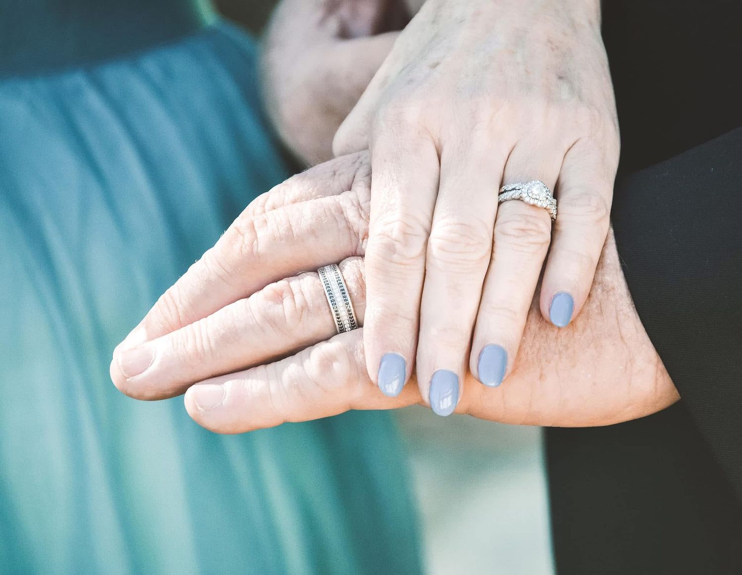 Close-up of hands with light blue nail polish and multiple silver rings against a turquoise background after a wedding.