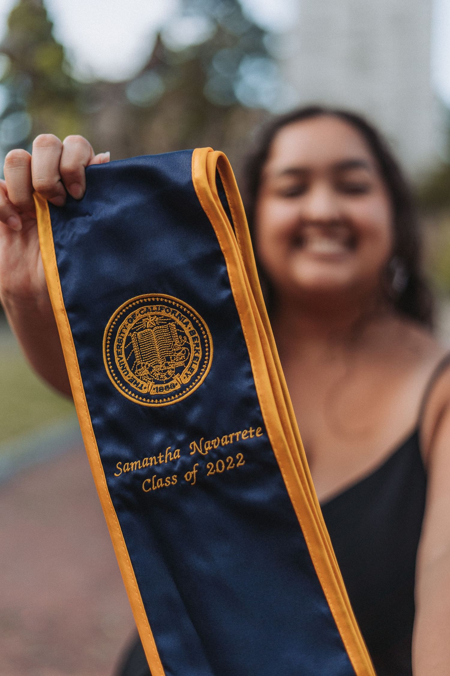 Smiling graduate holds UC Berkeley navy and gold stole embroidered with Samantha Navarrete Class of 2022.