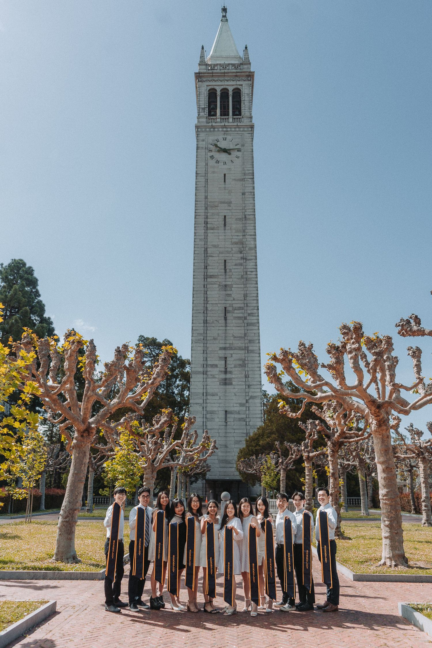 Large group of UC Berkeley graduates pose in front of the iconic Sather Tower on a sunny day.