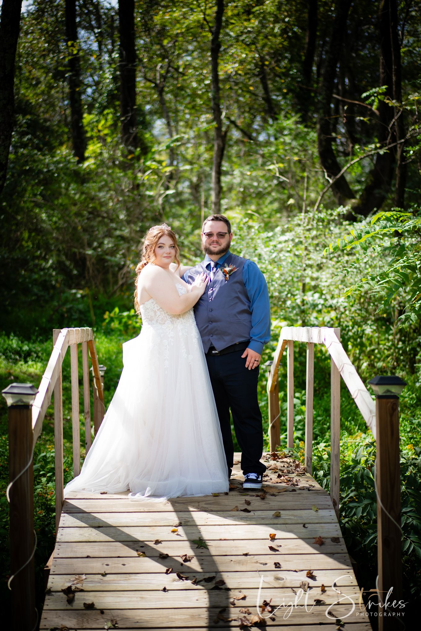 A couple stands together on a rustic wooden bridge surrounded by lush green foliage in a romantic outdoor North Carolina wedding.