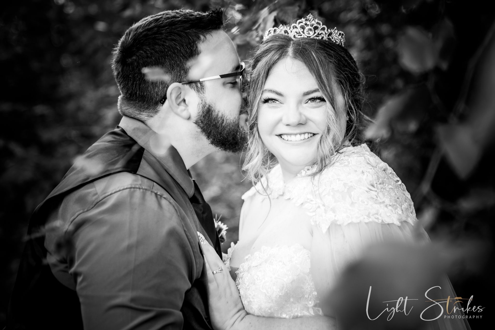 A black and white wedding photo showing a tender moment between newlyweds in a garden setting.