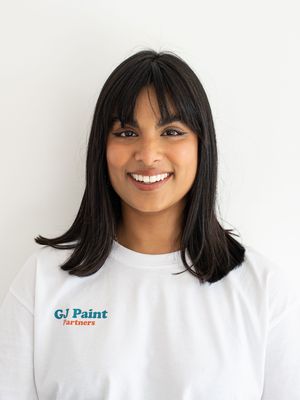 Person with dark bangs and shoulder-length hair smiling against white background wearing white top.