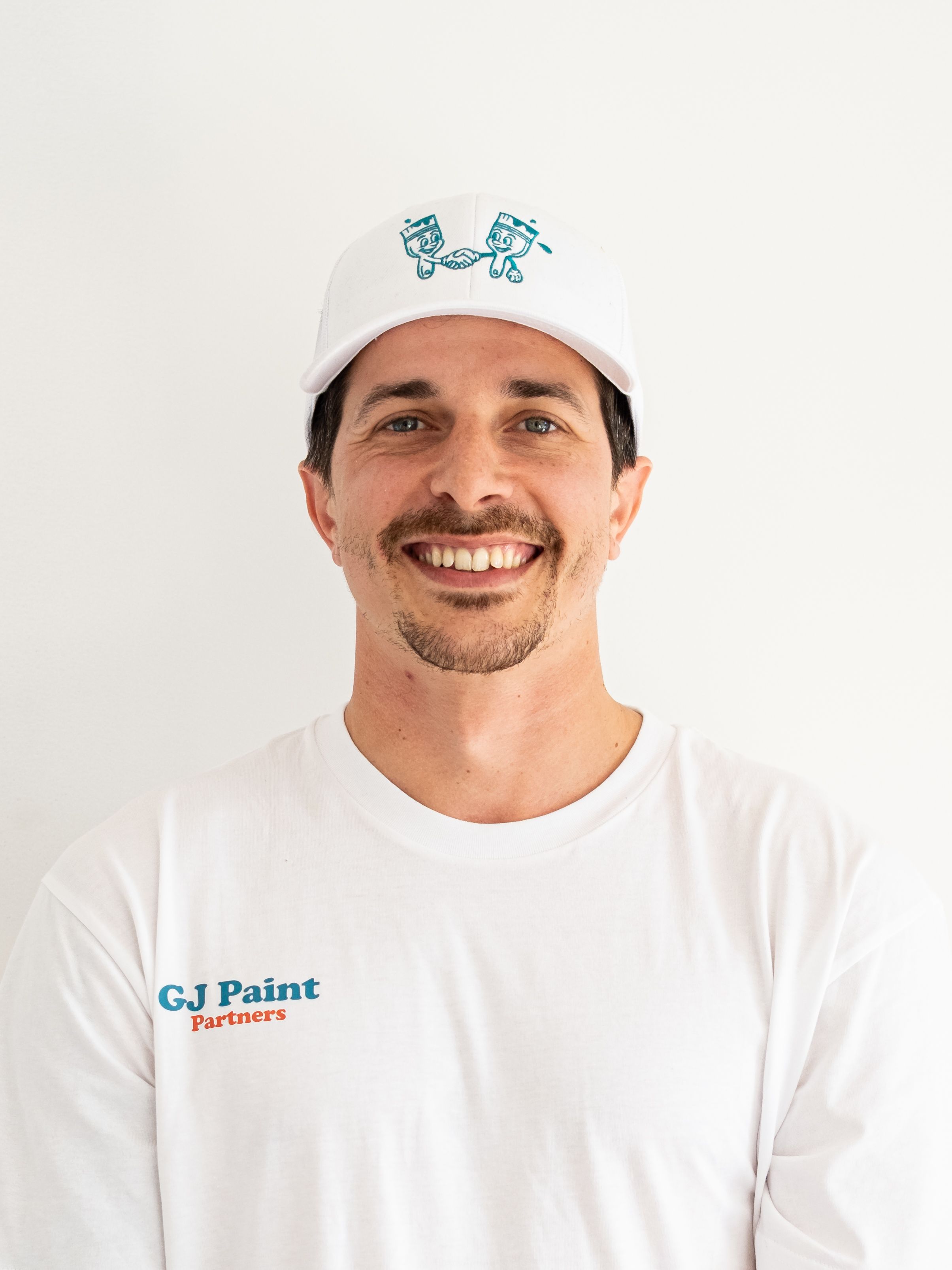 Professional painter in white uniform and branded cap smiling at camera against white background.