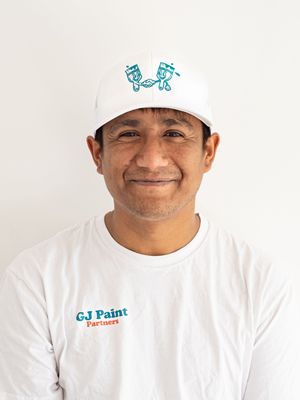 Professional painter in white uniform and cap with company logo smiling against white background.