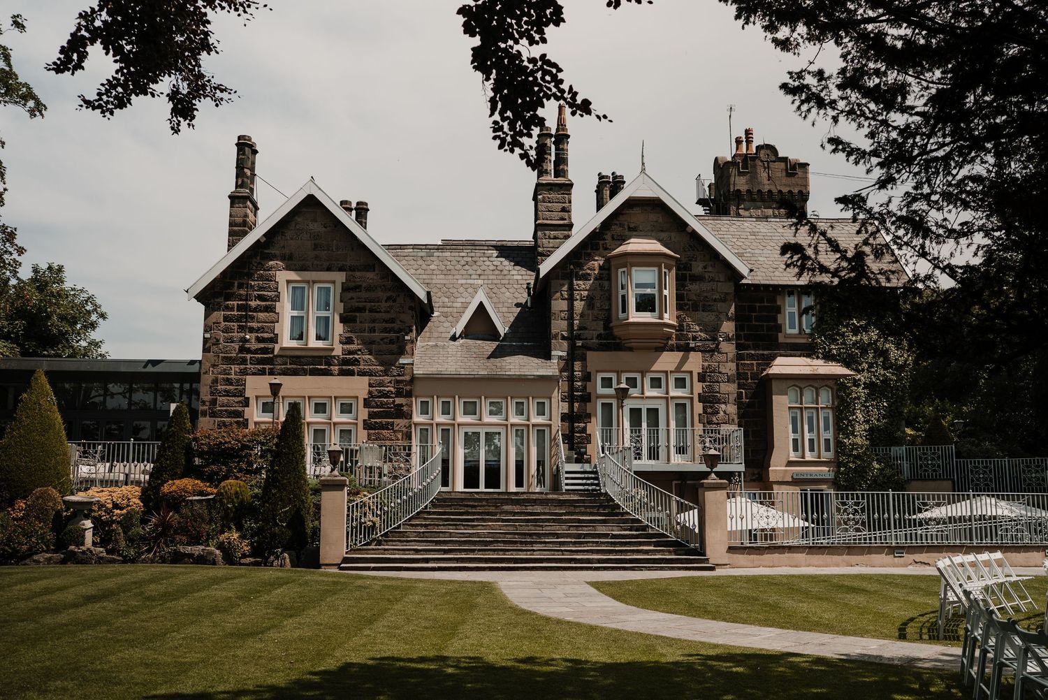 Stone mansion with Tudor-style architecture features multiple gables and chimneys surrounded by manicured gardens.