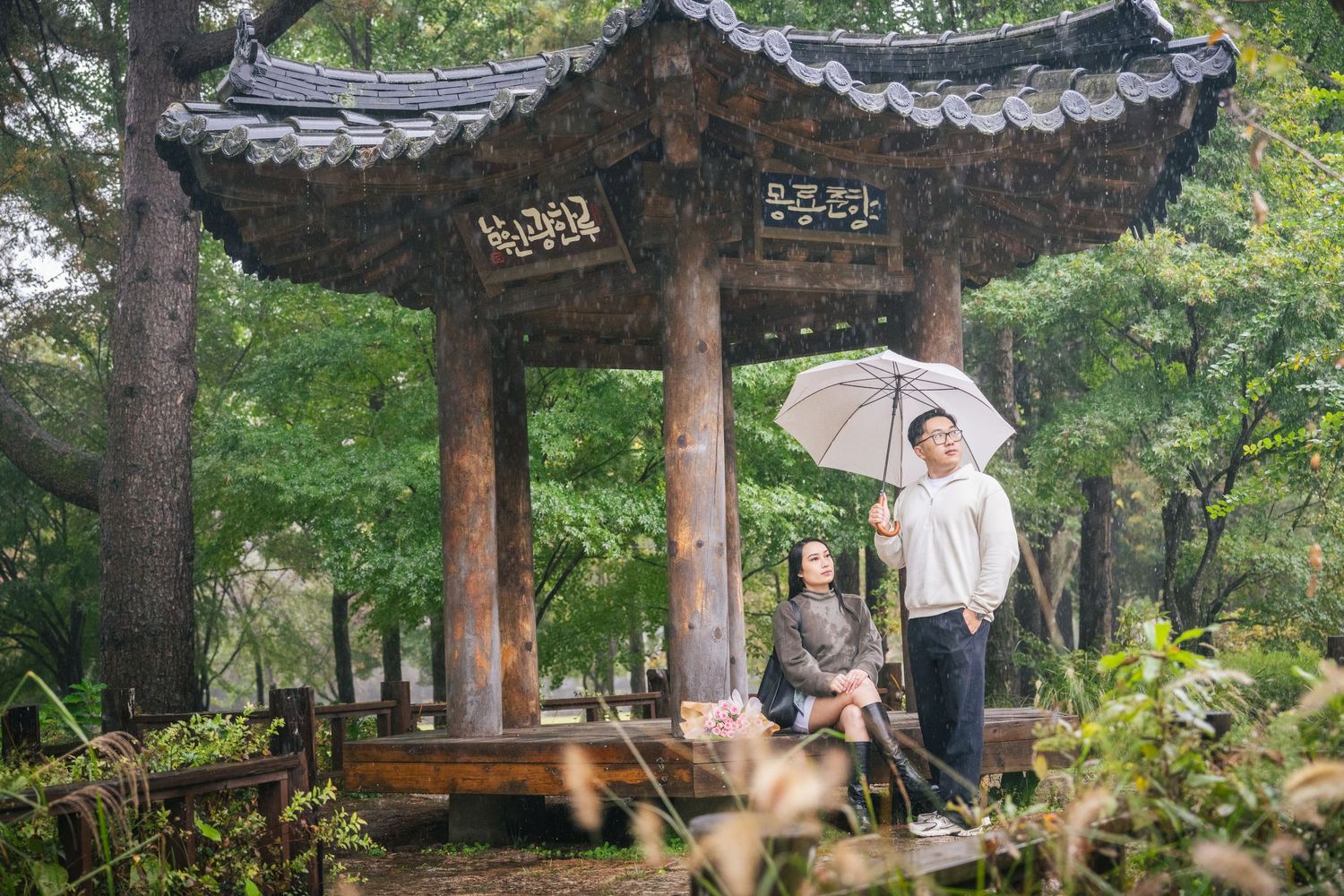Traditional Korean pagoda-style buildings with curved tile roofs stand among lush green trees in a peaceful garden setting.
