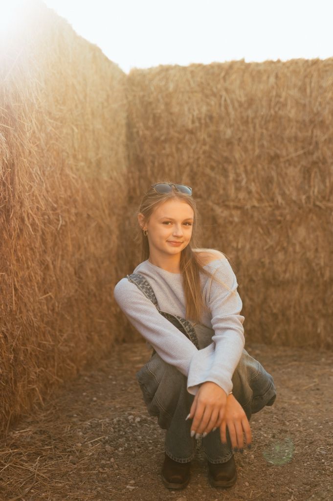 Rustic autumn portrait against straw bales featuring cozy casual wear and natural lighting.