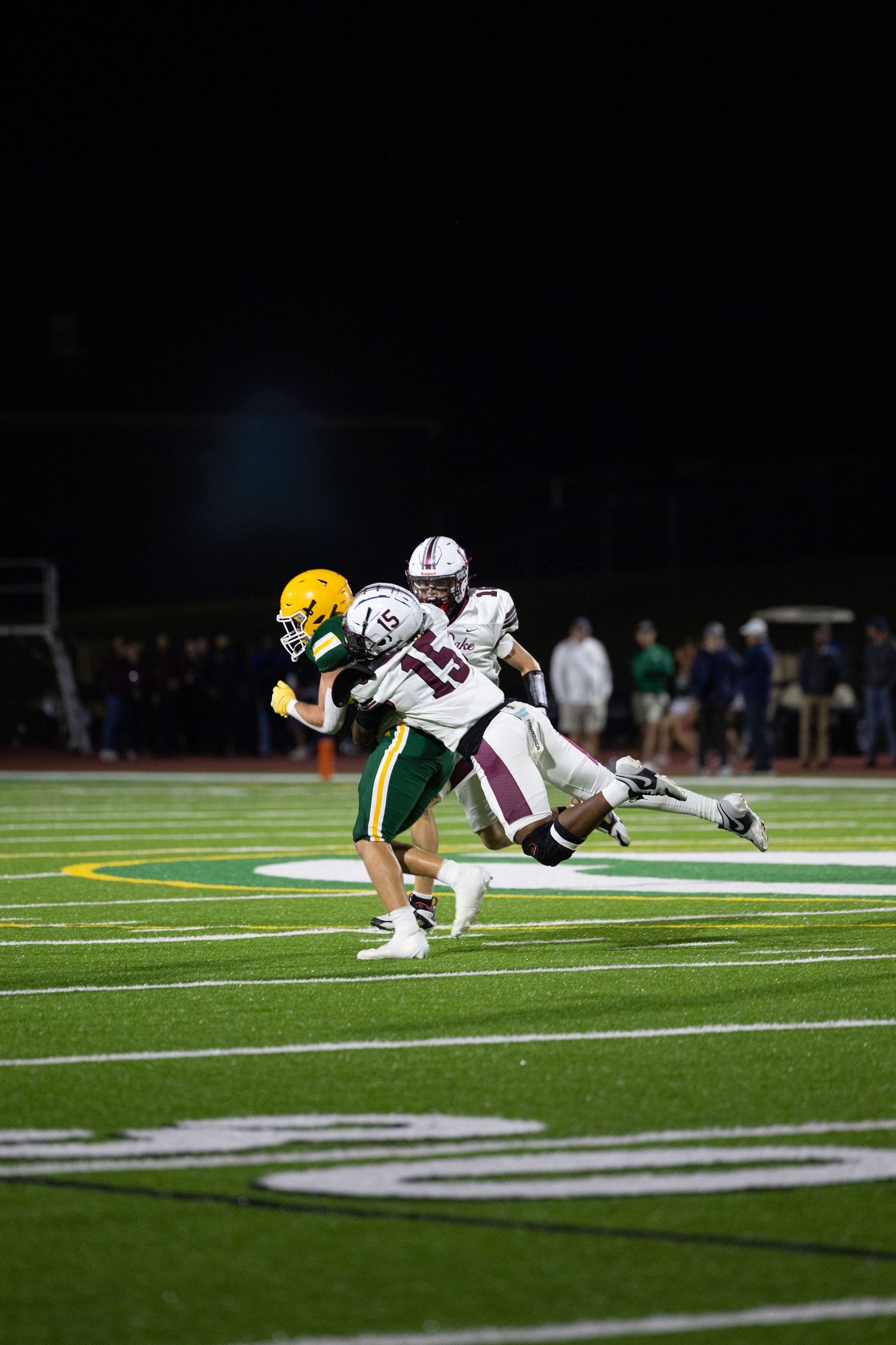 Football players dive and collide during a tackle attempt on the field during a night game.