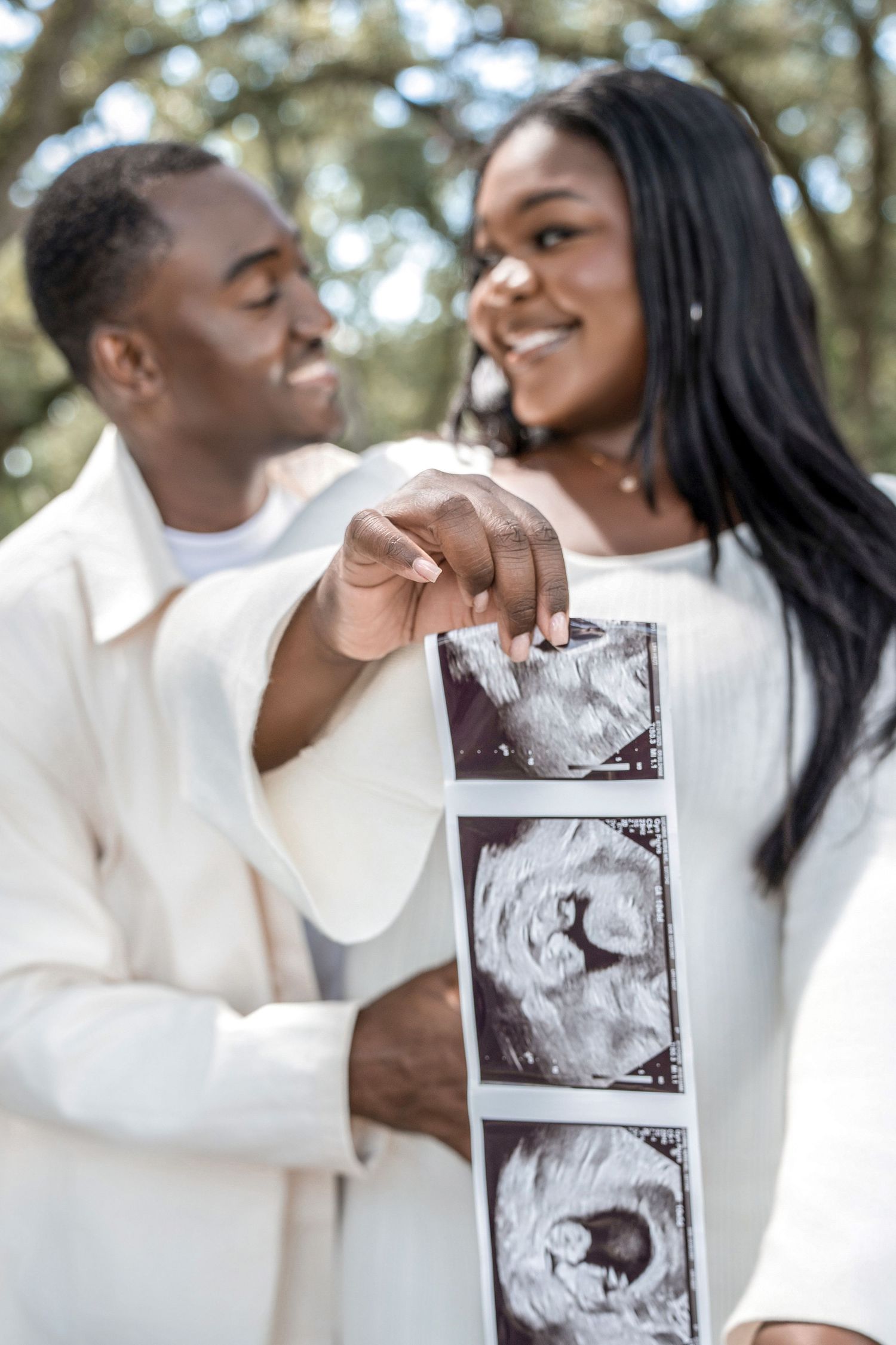 A couple in white sweaters share a joyful moment while holding ultrasound photos of their expected baby.