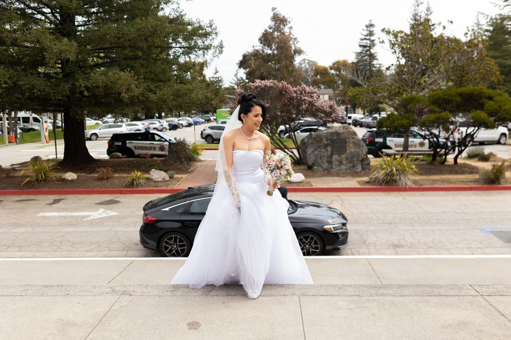 A bride in a flowing white wedding dress walks gracefully through a parking lot on an autumn day.